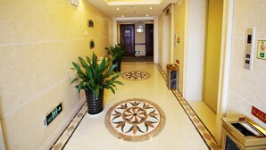 A hotel corridor with marble flooring, potted plants, an elevator, and a wall-mounted sign. - Vienna Hotel Chaoyang Road - Nanning (Nanning)