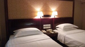 Une chambre d’hôtel avec deux lits, une table de chevet avec un téléphone et une lampe, et une tête de lit agrémentée de lampes fixées au mur.
