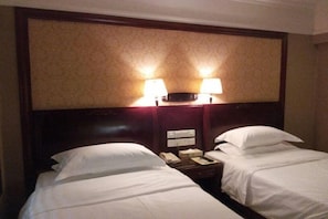 Une chambre d’hôtel avec deux lits, une table de chevet avec un téléphone et une lampe, et une tête de lit agrémentée de lampes fixées au mur.