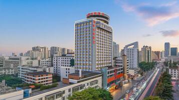 A high-rise hotel with multiple floors, surrounded by a cityscape with other buildings and a busy road with vehicles.