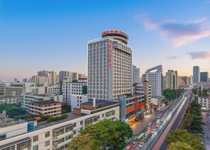 A high-rise hotel with multiple floors, surrounded by a cityscape with other buildings and a busy road with vehicles.