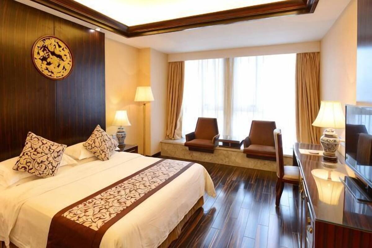Una habitación de hotel con una cama grande, dos mesitas de noche con lámparas, un televisor, un sofá y una ventana con cortinas.