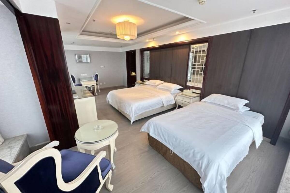 Una habitación de hotel con dos camas, una mesita, una silla y un espejo.