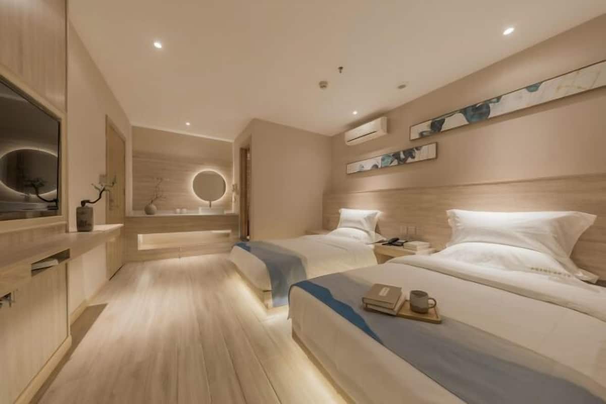 A modern hotel room with two beds, a wooden floor, a built-in TV, and a circular mirror.