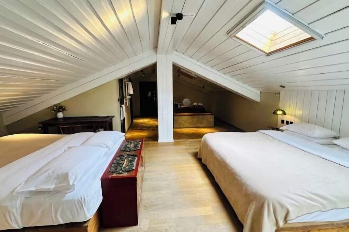 Ein Schlafzimmer mit zwei Betten, einer hölzernen Bank, einem Oberlicht und einer Treppe zu einer Erkerzone.
