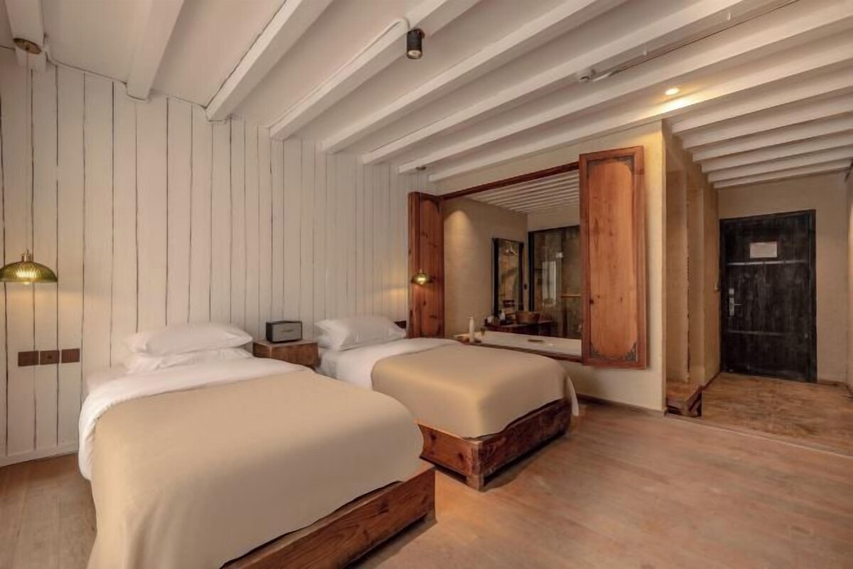A bedroom with two beds, wooden headboards, a large mirror, and a wooden door.