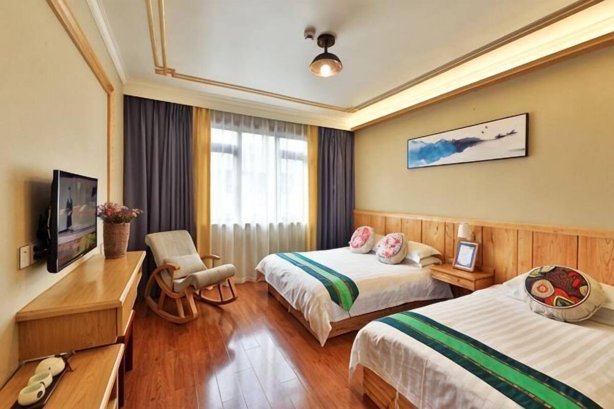 Ein Hotelzimmer mit zwei Betten, einem Schreibtisch, einem Stuhl, einem Fernseher und einem Fenster mit Vorhängen.