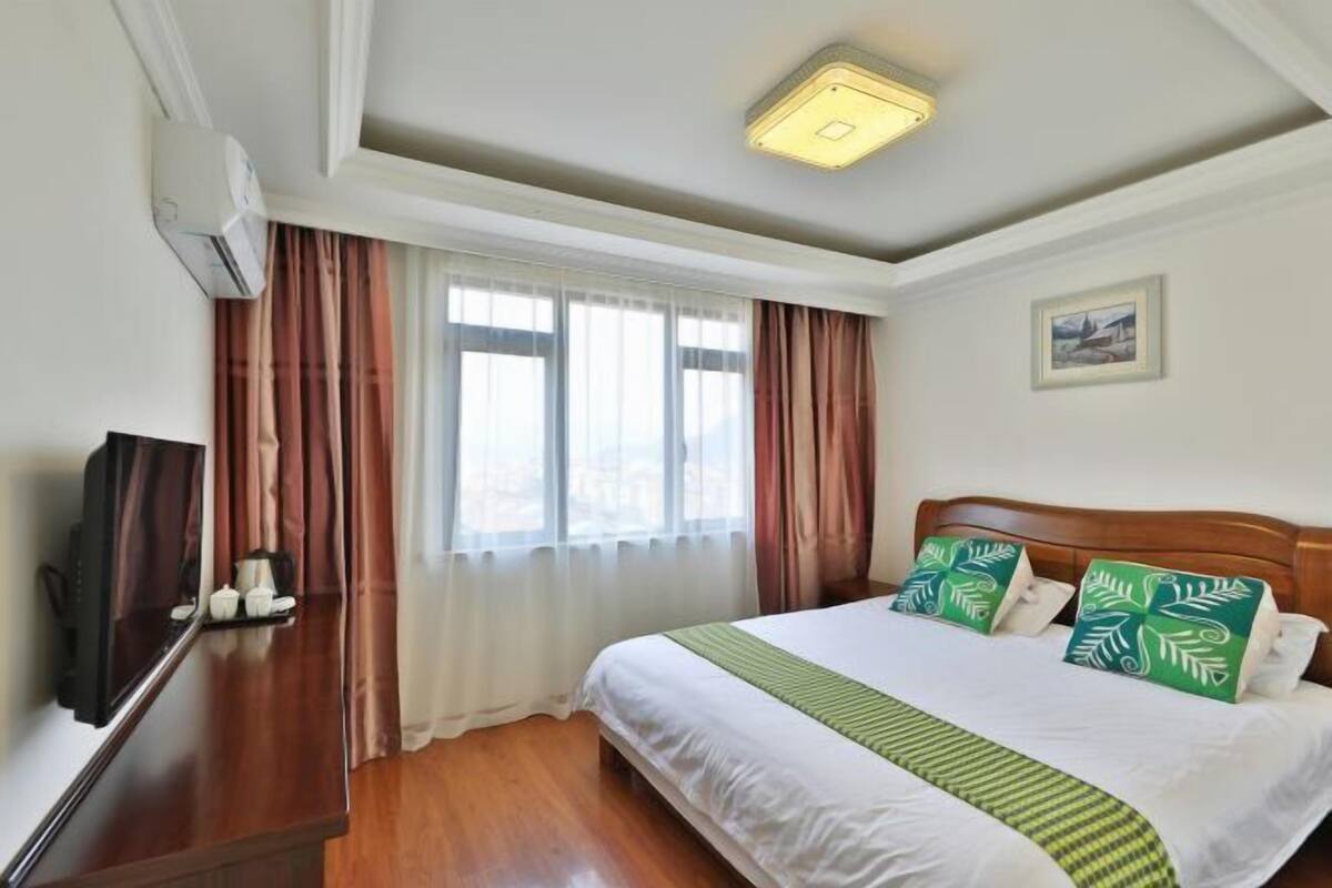 Ein Hotelzimmer mit Bett, Fernseher, Schreibtisch und einem Fenster mit Vorhängen.