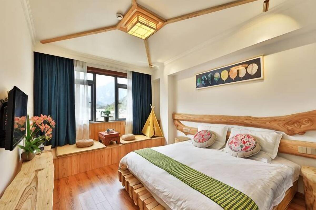 Ein Schlafzimmer mit Bett, einem Fenster mit Vorhängen, einem Bild an der Wand und einem hölzernen Kopfteil.