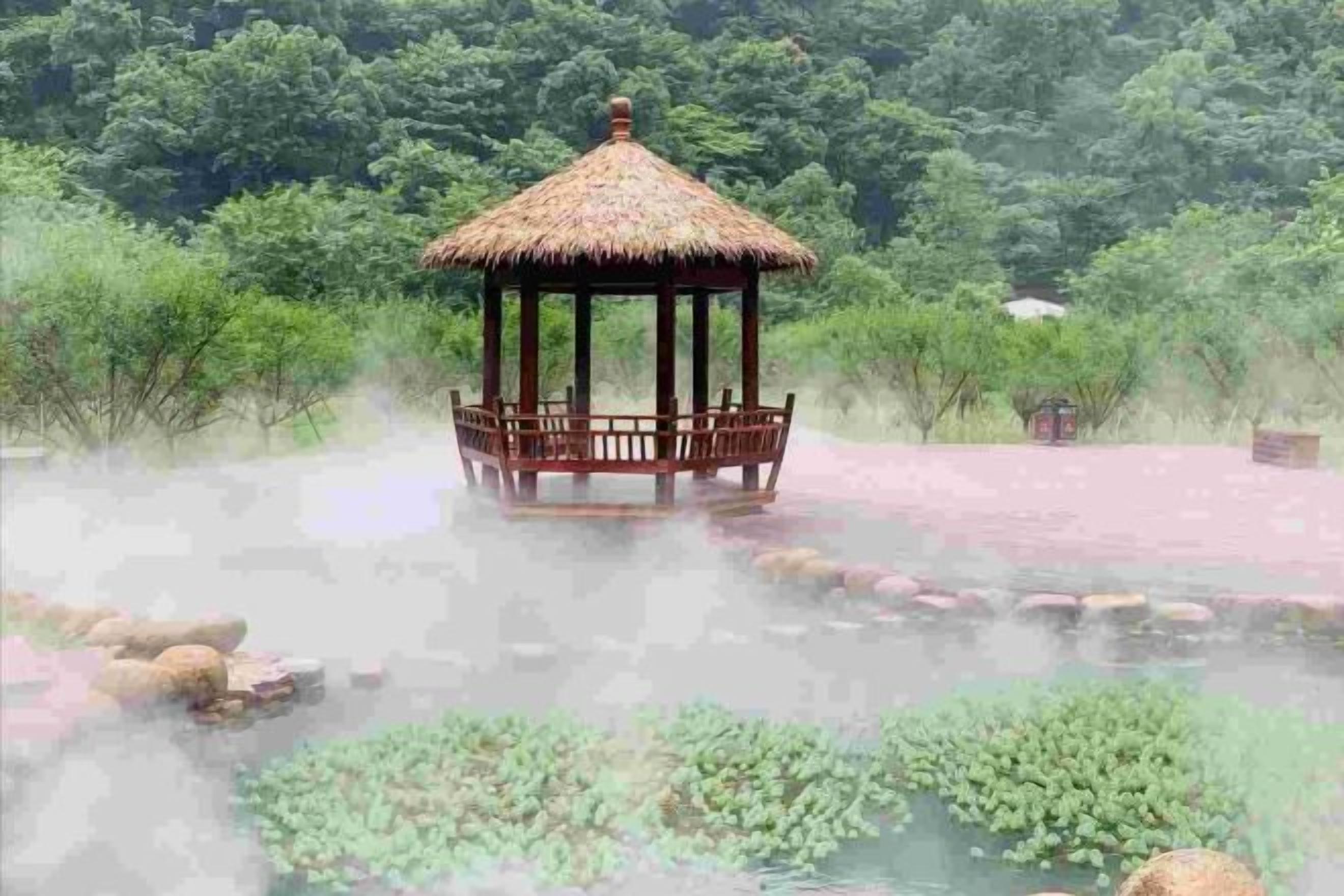 A gazebo with a thatched roof, surrounded by a body of water with lily pads and rocks.