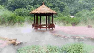 A gazebo with a thatched roof, surrounded by a body of water with lily pads and rocks.