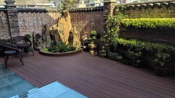 Una terraza de madera con un muro de ladrillo, plantas en macetas y un elemento decorativo de piedra.
