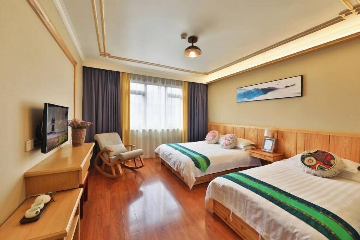 Ein Hotelzimmer mit zwei Betten, einem Schreibtisch mit Stuhl, einem Fernseher und einem Fenster mit Vorhängen.