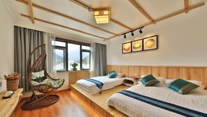 Una habitación de hotel con piso de madera, dos camas con almohadas azules y verdes, una mecedora, una ventana con cortinas y una lámpara fijada a la pared.