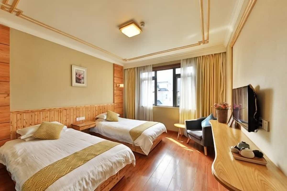 Ein Hotelzimmer mit zwei Betten, einem Schreibtisch, einem Stuhl, einem Fernseher und einem Fenster mit Vorhängen.