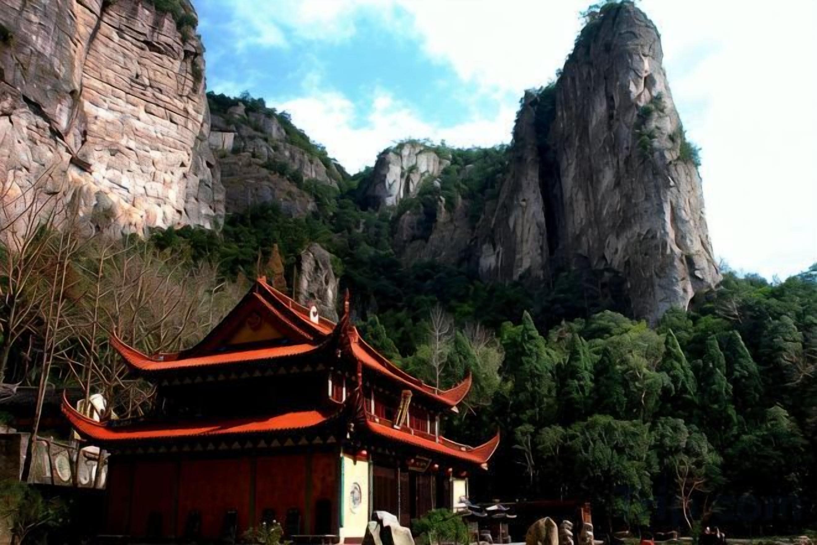 A traditional building with a red roof and multiple eaves, situated in a natural setting with a prominent rock formation in the background.