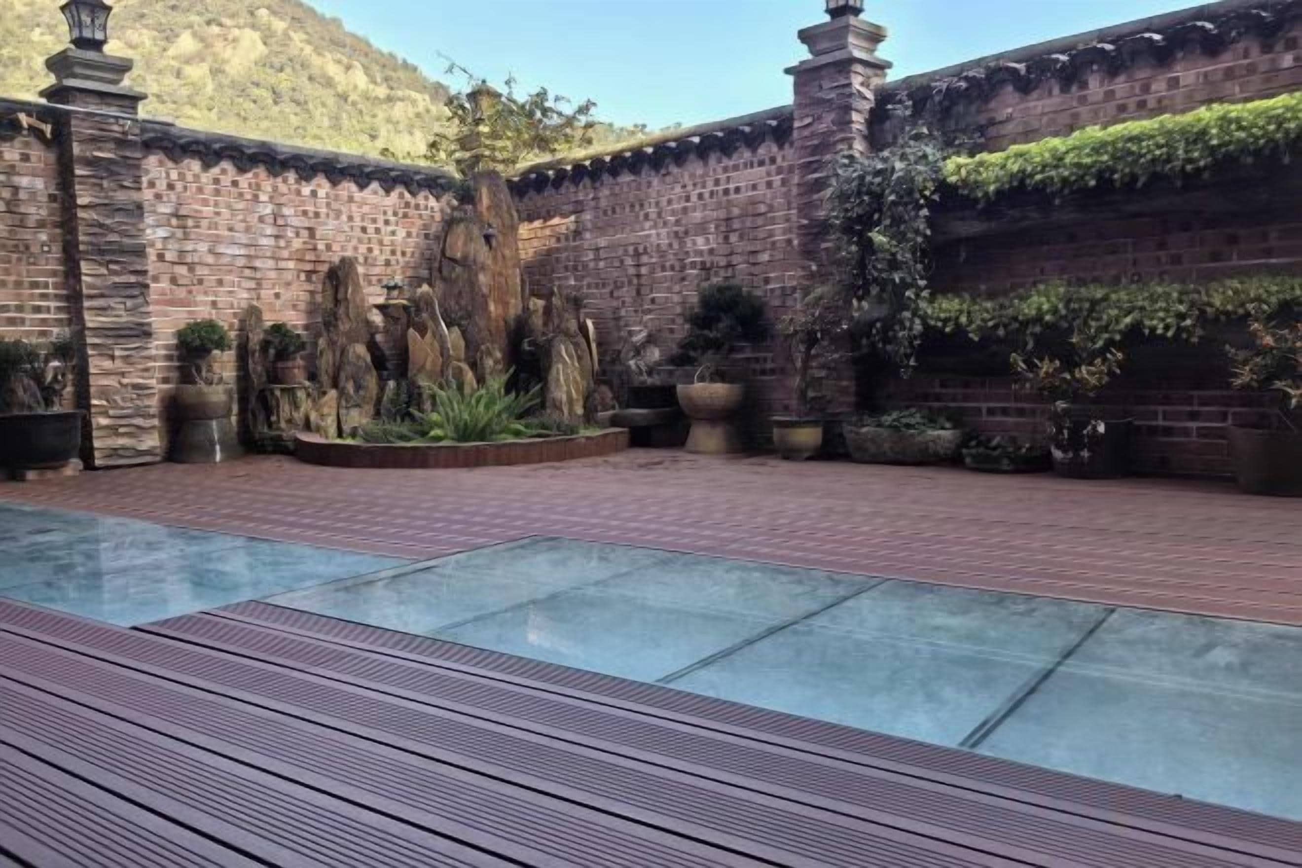 Une cour avec une piscine à débordement en verre, des murs en briques et des plantes en pot.