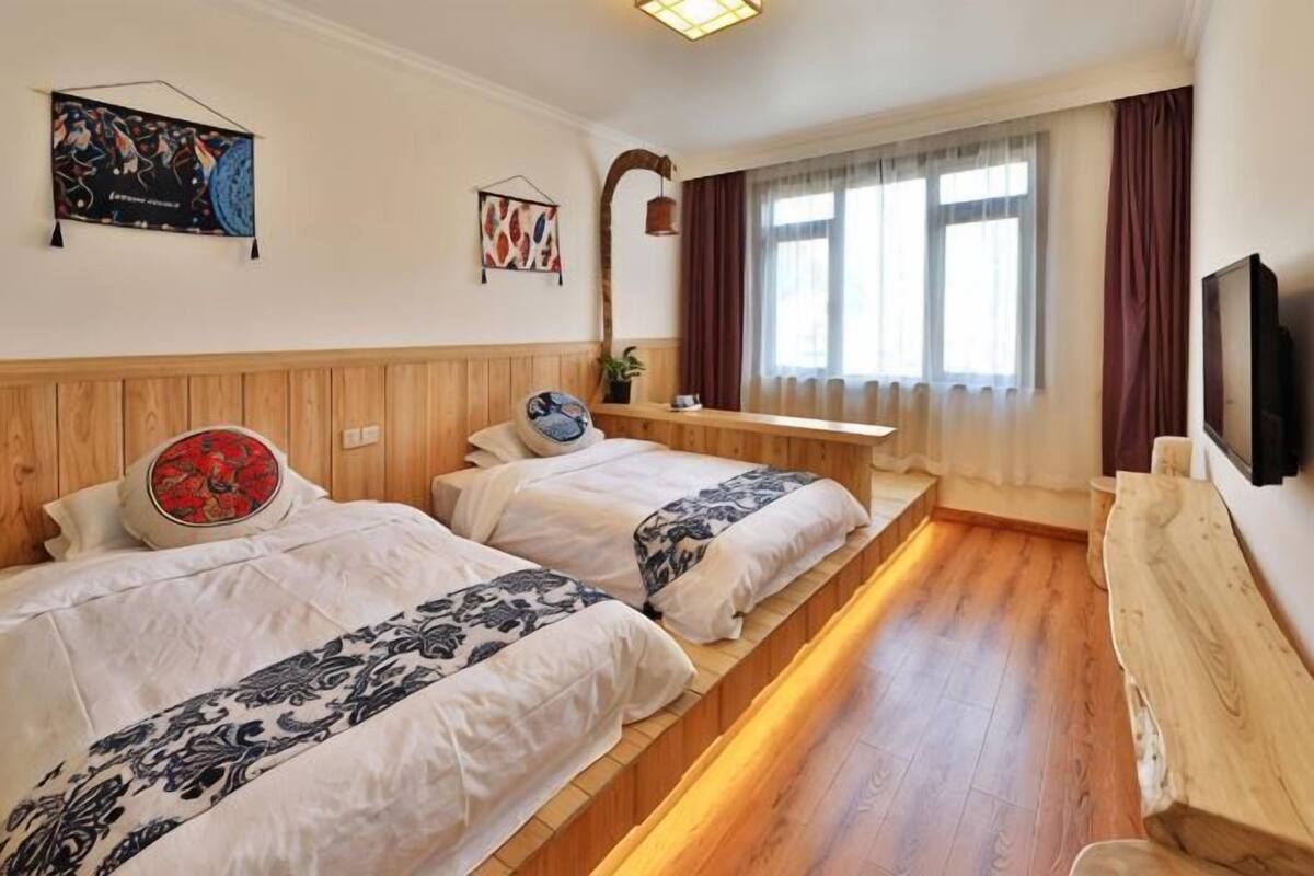Ein Hotelzimmer mit zwei Betten, einem hölzernen Kopfteil, einem Flachbildfernseher und einem Fenster mit Vorhängen.