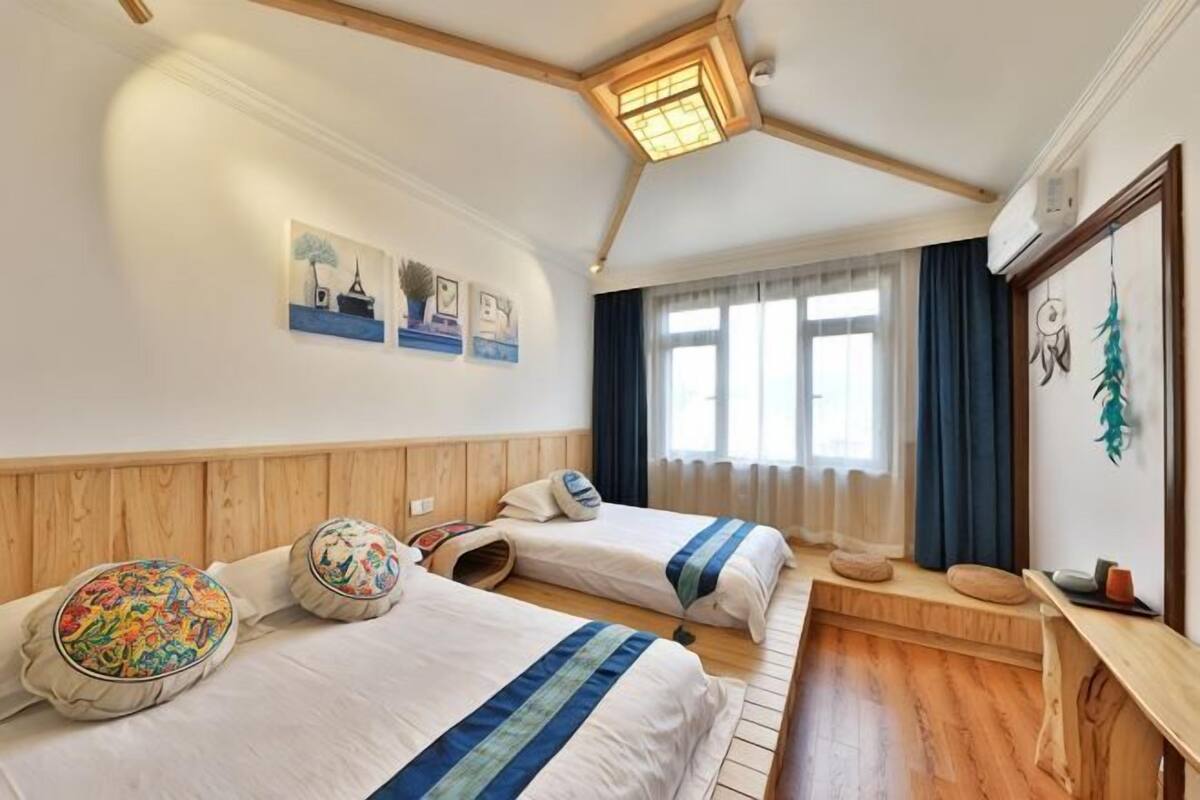Ein Hotelzimmer mit zwei Betten, einer hölzernen Bank, einem Schreibtisch und einem Fenster mit Vorhängen.