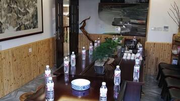Un salón de conferencias con una larga mesa, botellas de agua, una planta en maceta y un cuadro en la pared.