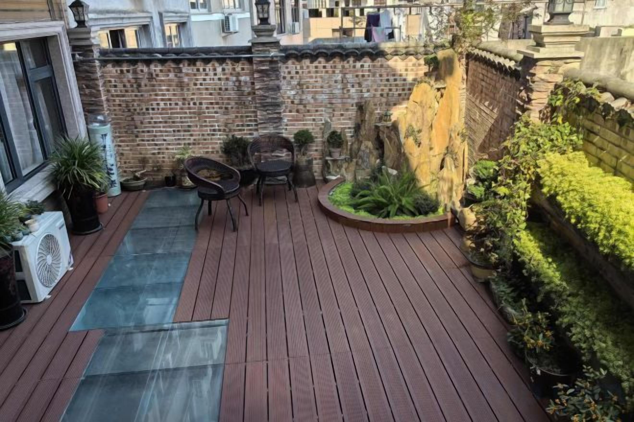 A rooftop terrace with a wooden deck, a small seating area, and potted plants.