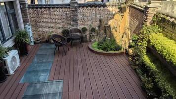 A rooftop terrace with a wooden deck, a small seating area, and potted plants.