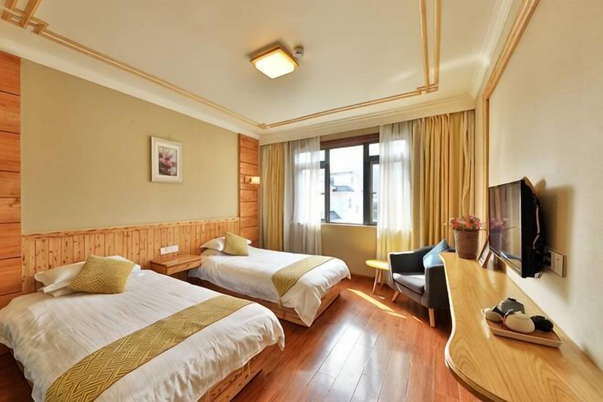 Ein Hotelzimmer mit zwei Betten, einem Schreibtisch, einem Stuhl, einem Fernseher und einem Fenster mit Vorhängen.