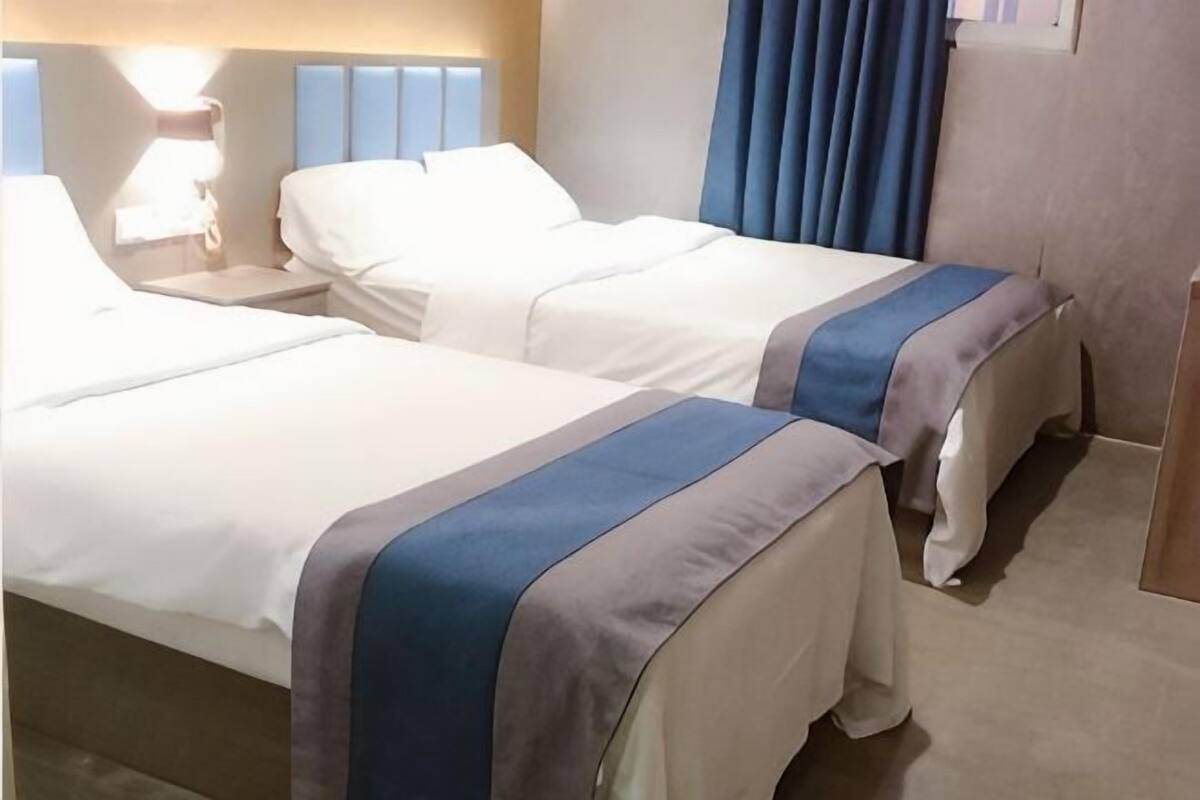 A hotel room with two beds, a nightstand, a lamp, and a window with curtains.