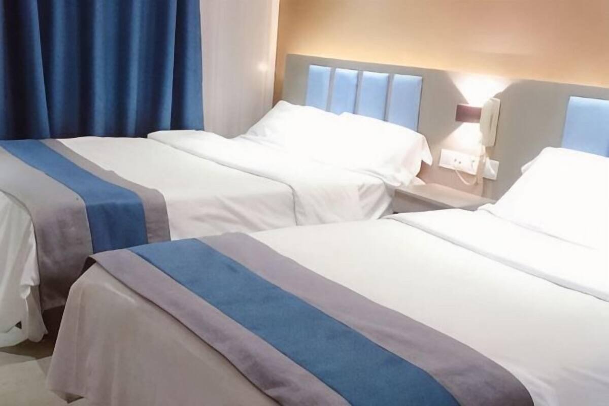 Two beds with white linens and blue stripes, a bedside table with a lamp, and a window with blue curtains.