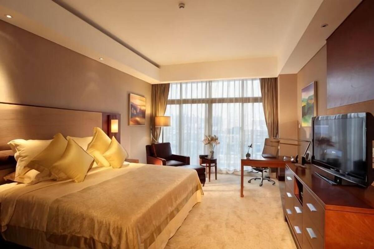 Una camera d'albergo con un letto grande, una scrivania, una sedia, una televisione e una finestra con tende.