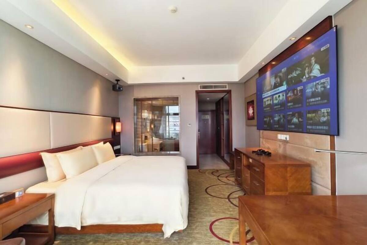 Una camera d'albergo con un letto, una scrivania, una TV e un bagno visibile attraverso una porta in vetro.