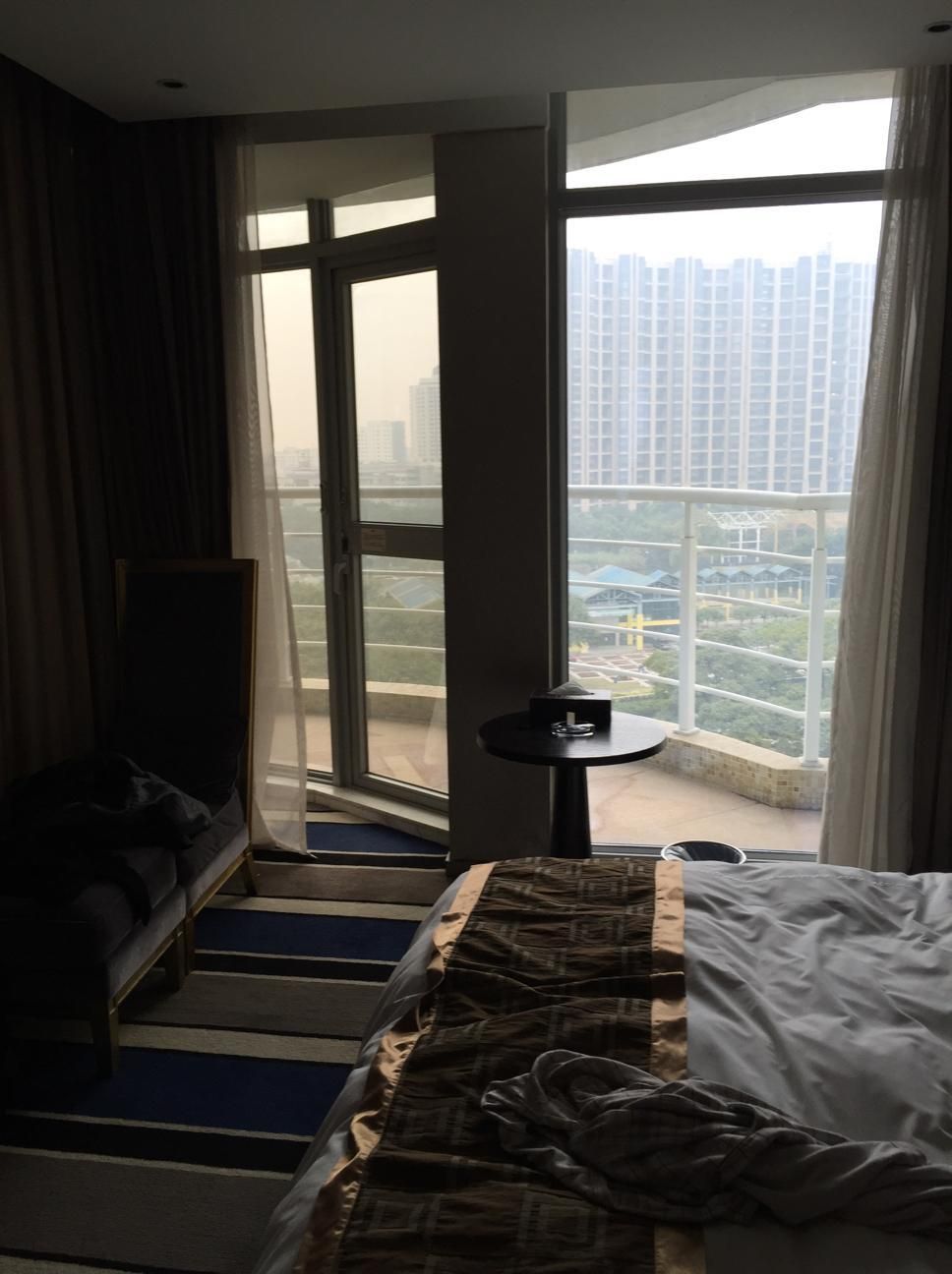 Habitación de hotel con cama, una mesita y vista a un paisaje urbano a través de amplias ventanas.