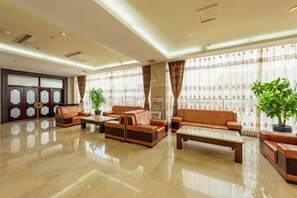 Un vestíbulo amplio con zona de estar, mostrador de recepción y ventanas grandes con cortinas.