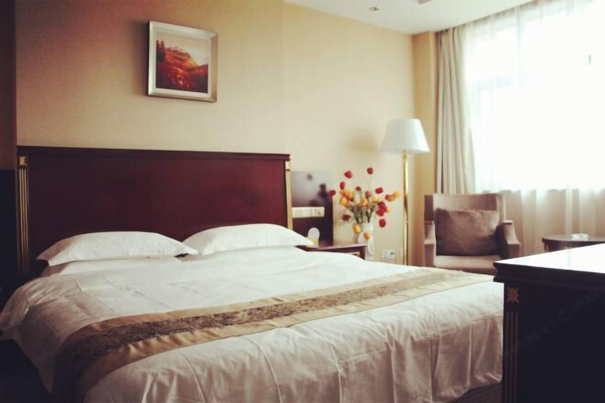 Een hotelkamer met een groot bed, een nachtkastje met lamp, een stoel en een bureau.