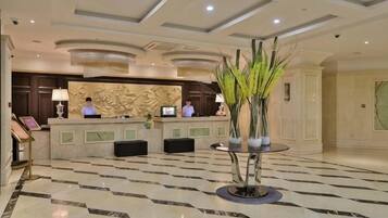 A hotel reception area with a marble floor, reception desk, and two receptionists.