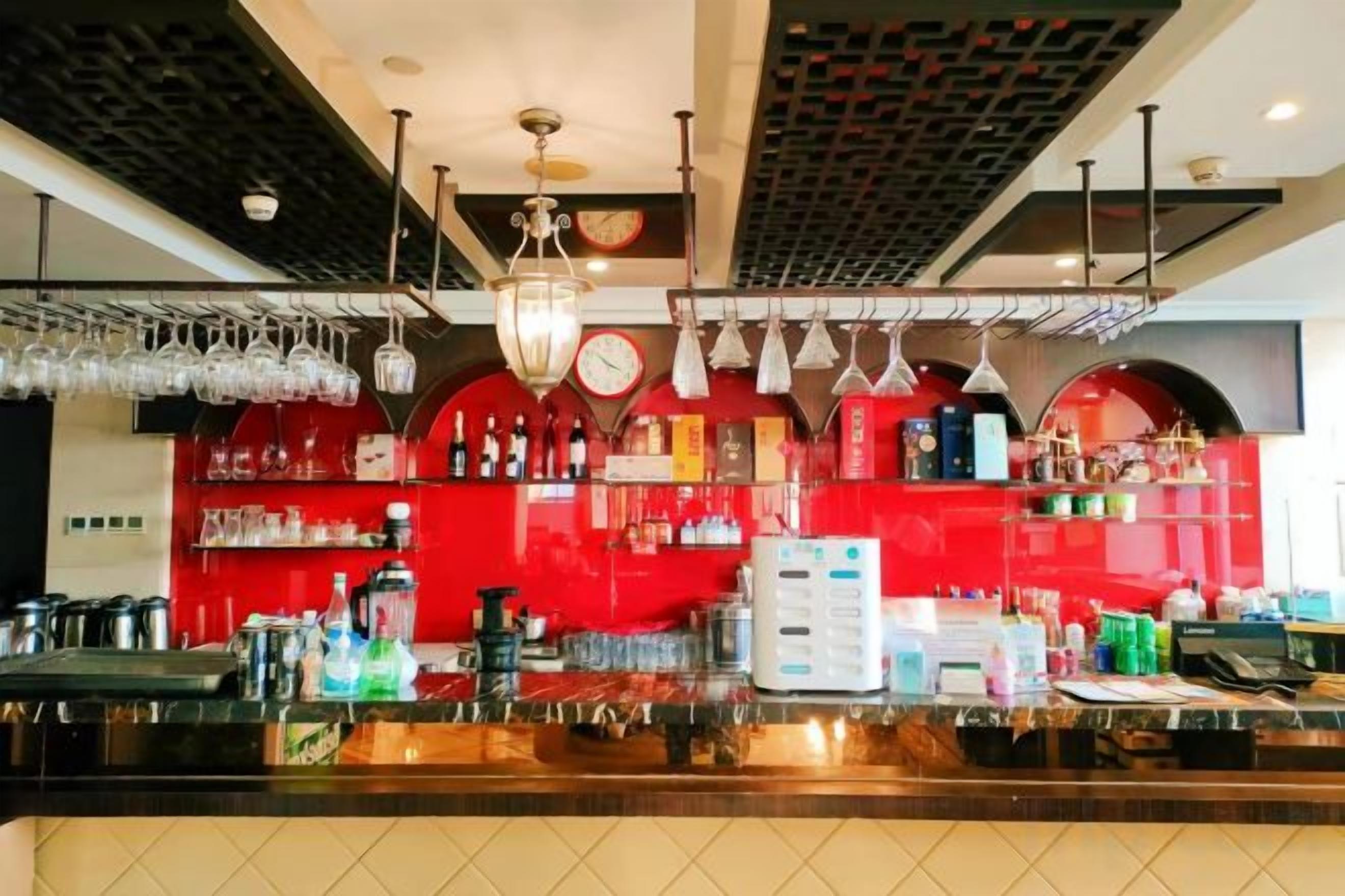 A bar area with a red wall, hanging lights, and various bar equipment.