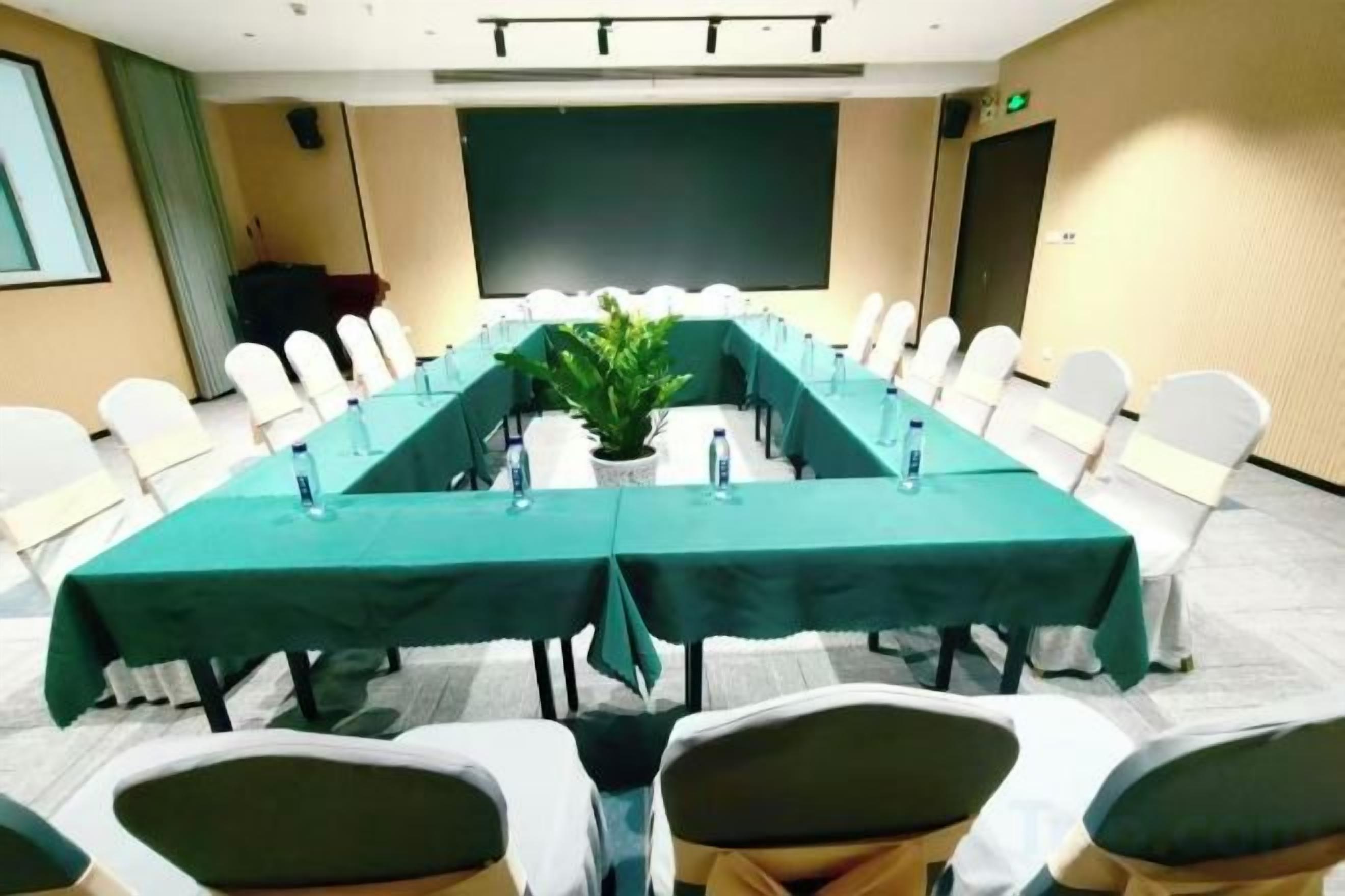 Un salón de conferencias con una larga mesa, sillas y una pantalla de proyector.