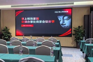 A conference room with a large screen displaying text, rows of tables with chairs, and water bottles on each table. - Jiaqi Landscape Hotel (Chizhou)