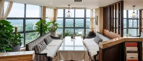 A dining area with a high table and benches, large windows, and a view of the outdoors.