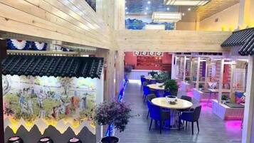 Un restaurante con techo alto, vigas de madera y un pasillo central. Mesas y sillas están dispuestas a lo largo de los laterales.