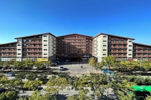A multi-story hotel with a central courtyard, surrounded by trees and a parking area.