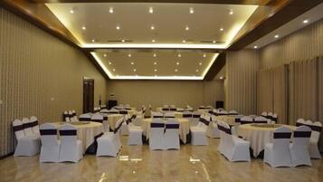 A large conference room with round tables and white chairs, each with a dark sash. The room has a high ceiling with recessed lighting and a polished floor.
