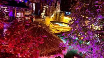 A tropical-themed outdoor area with a thatched-roof structure, seating, and a pool area.