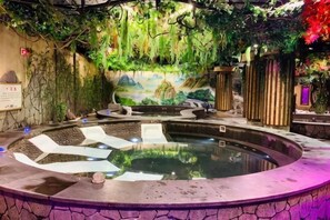 A hot tub with a circular design, surrounded by a stone pool and a decorative wall with greenery.