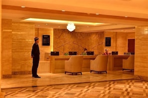 A hotel reception area with a uniformed staff member, a reception desk, and a modern chandelier.