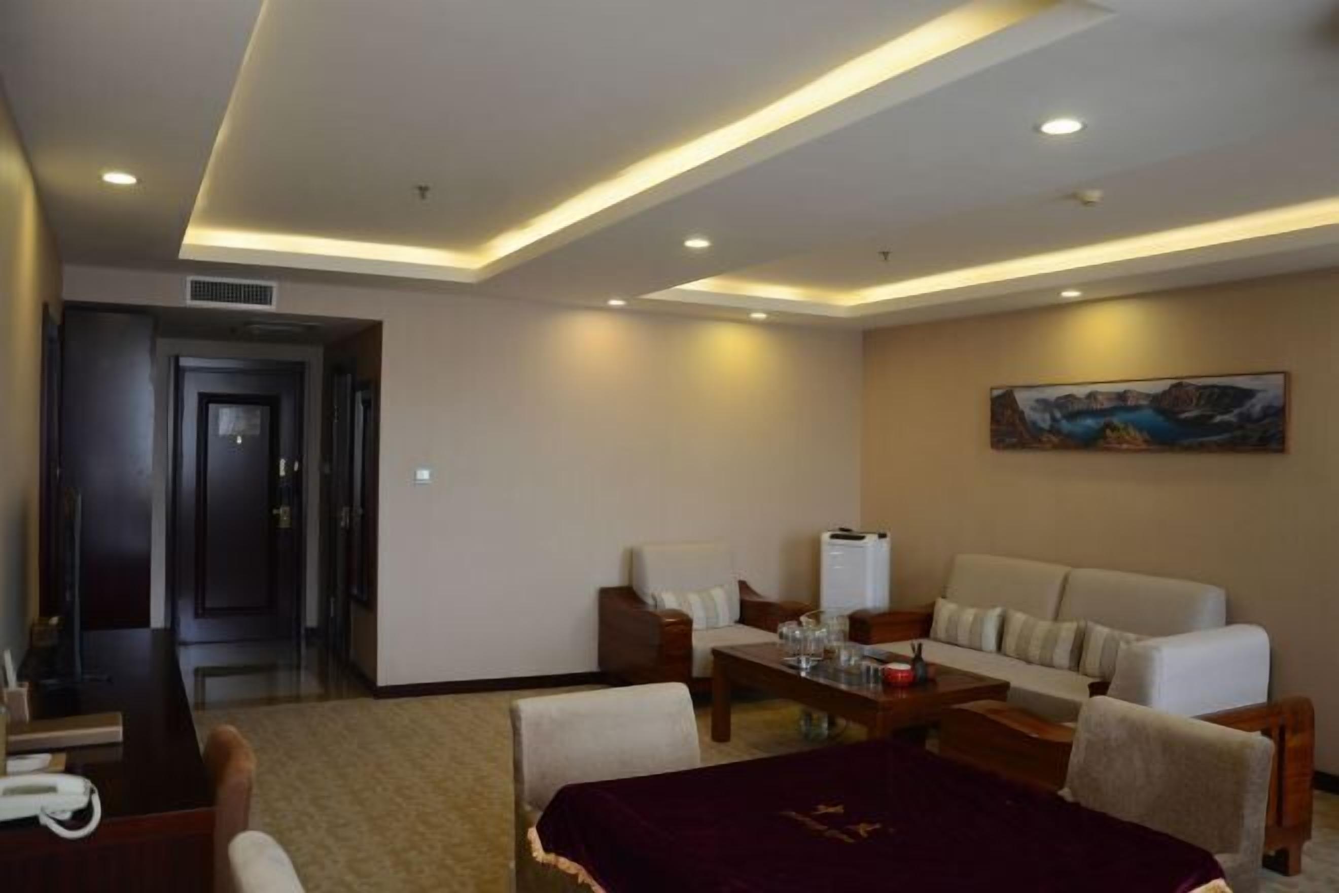 A hotel room with a dining area, a sofa, a coffee table, and a painting on the wall.