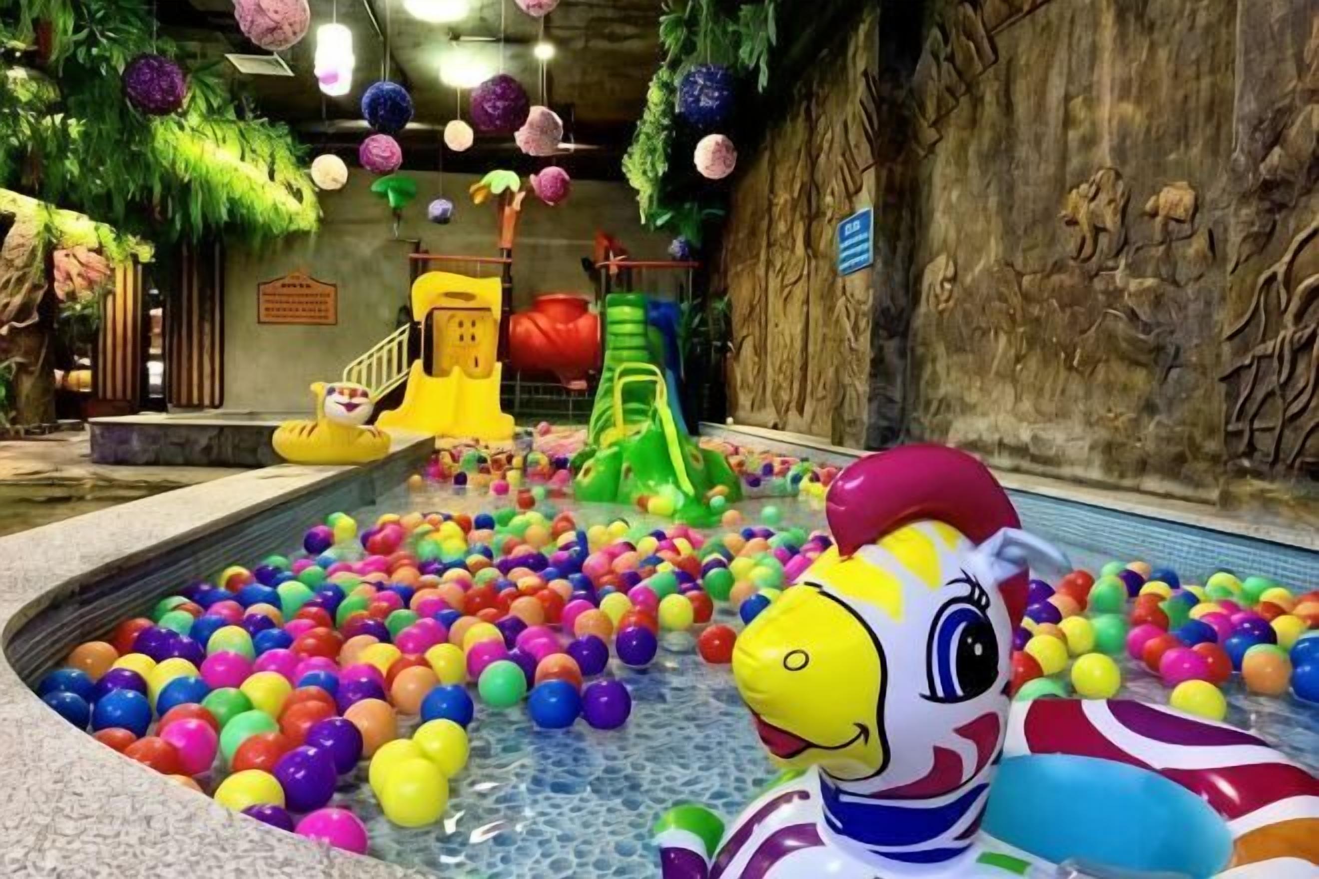 An indoor play area with a pool filled with colorful plastic balls, a yellow slide, and a green slide.