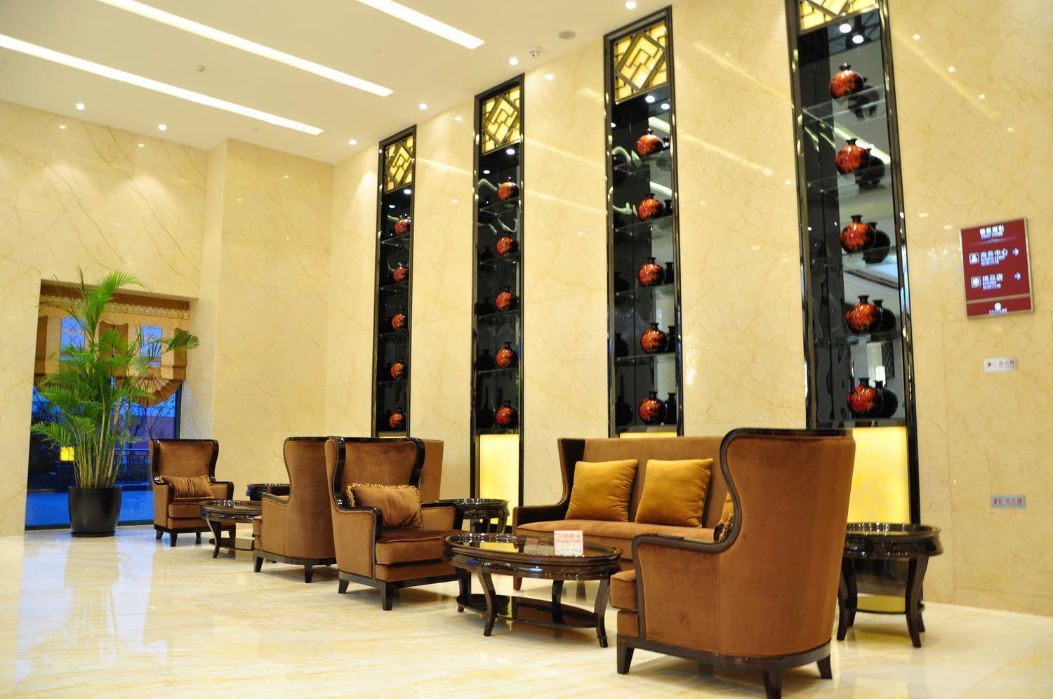 A lobby with seating arrangements, a large potted plant, and decorative vases on shelves.