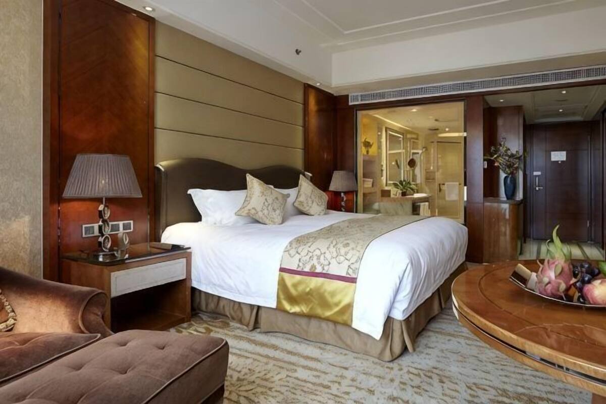 Een hotelkamer met een groot bed, een nachtkastje, een lamp, een stoel en een schaal fruit.