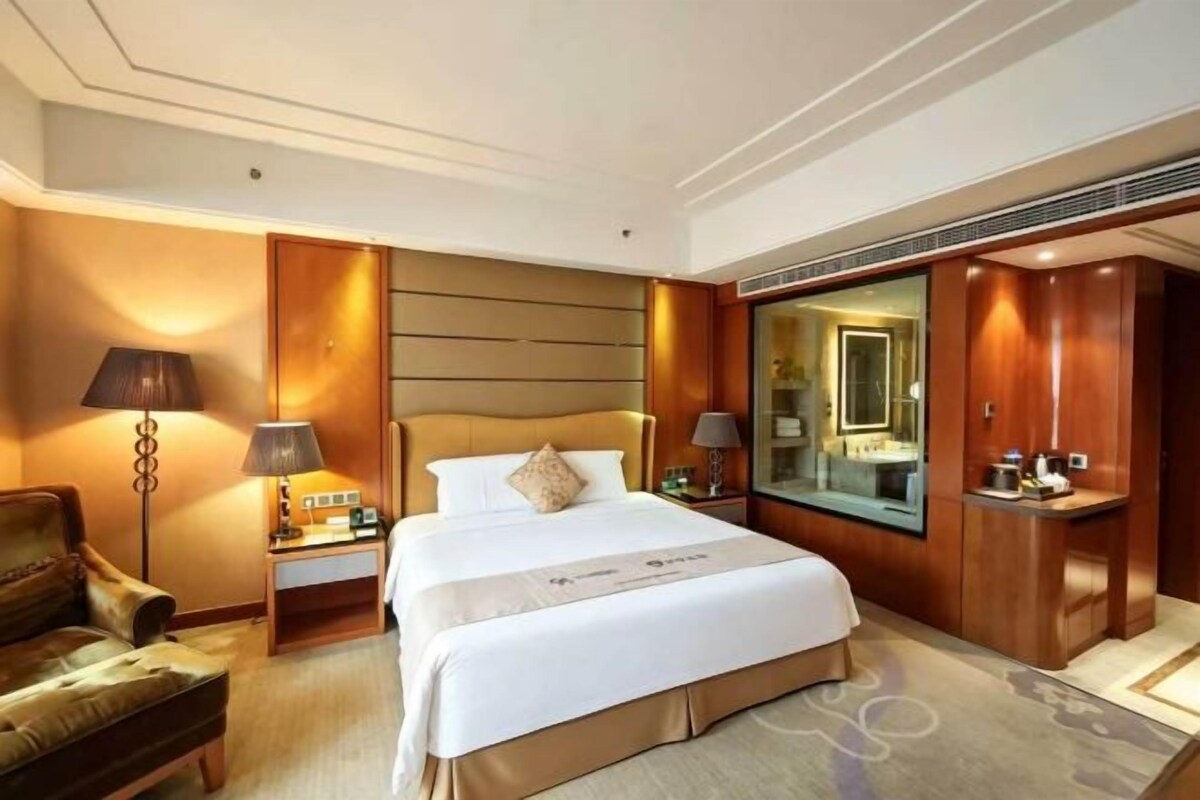A hotel room with a large bed, bedside tables, a chair, a mirror, and a wardrobe.